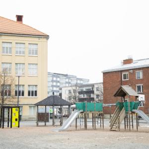 Vasemmalla vanhaa koulua, oikealla uudempaa, etualalla leikki- ja liikuntavälineitä.