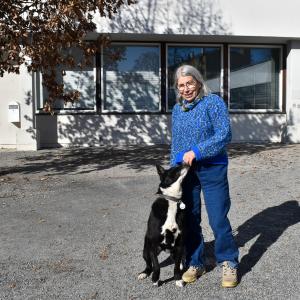 A person stands in front of the school with their dog. The dog sniffs the owner&#039;s hands.