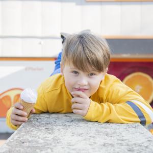 Keltapuseroinen poika nojaa pöytään ja syö jäätelöä.