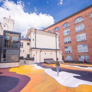 Värikäs katumaalaus Finlaysonin tiilirakennusten välissä, yksittäisiä ihmisiä kulkee alueella.