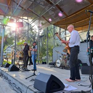A jazz band of middle-aged men performs on an outdoor stage in sunny weather.