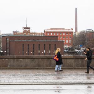 Kolme henkilöä kävelemässä vastakkaisiin suuntiin Hämeensillalla, taustalla Tammerkosken putous ja voimalaitos.