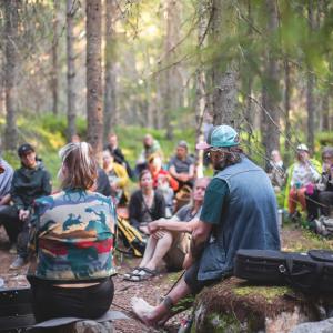 A large group of people are sitting in the Kintulammi forest listening to a musical performance.