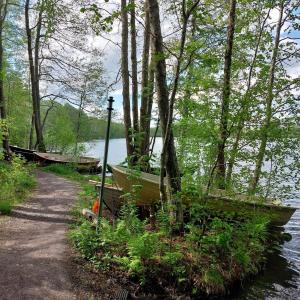 Järven rannalla soutuveneitä ja kapea hiekkapolku läpi lehtipuumetsän.