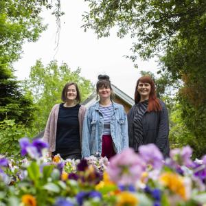  Liisa Aholainen, Janina Ahlfors ja Mirjam Larinkari katsovat kameraan kukkapenkkien takaa.