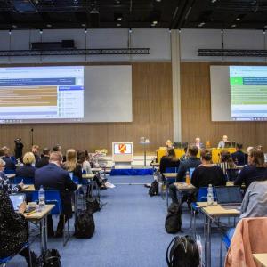 Ihmisiä takaa istumassa, edessä esitys ja henkilöitä.