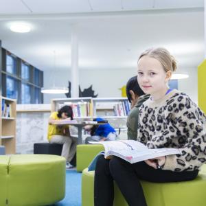 Nuori oppilas istuu kirja sylissä koulun tiloissa.