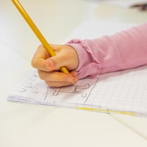 Pienen lapsen käsi piirtämässä lyijykynällä vihkoon