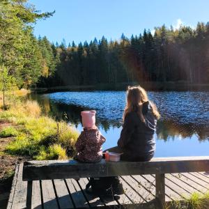 Lapsi ja nainen istuvat auringossa laiturin penkillä katsellen järvelle.
