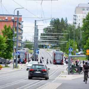 Henkilöautoja, ratikoita, pyöräilijöitä ja kävelijöitä Hervannan keskustassa.