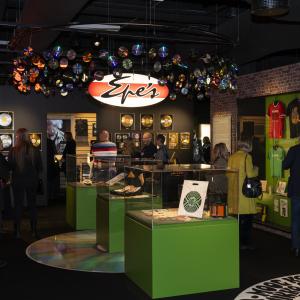 Manserock-näyttelyssä ihmisiä tutustumassa näyttelyyn. Hämärässä näyttelytilassa on keskellä tilaa vitriineitä, seinillä kultalevyjä.