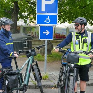 Kaksi henkilöä seisoo pyörien vieressä pysäköintimerkin edessä ja katsovat toisiinsa.