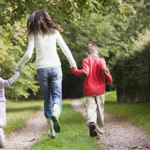 Aikuinen ja kaksi lasta juoksevat käsi kädessä kesäisellä metsäpolulla.
