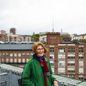 Henkilö seisoo kattoterassilla takanaan punatiilinen Tampellan vanha tehdasrakennus, jossa on iso Tamperella-kyltti katolla.