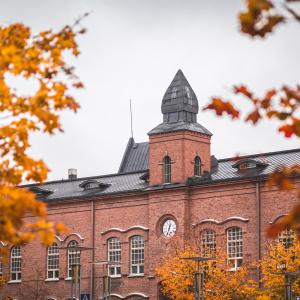 Punatiilinen rakennus ja sen kellotorni. Etualalla syksyisten puiden oksia.