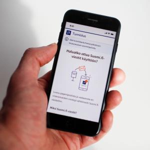 A person holding a mobile phone with instructions on how to activate Suomi.fi messages displayed on the screen.