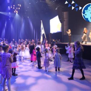 Lapsia tanssimassa lavan edessä. Lavalla tanssinohjaajia opastamassa tanssimaan. 