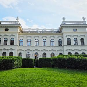 Museo Milavida kuvattuna Näsijärven puolelta. Vaalea kolme kerroksinen kivirakennus, edustalla vihreitä pensaita ja nurmikkoa. 