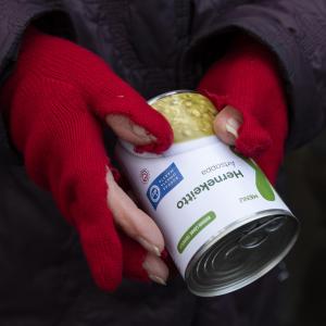 Hernekeittopurkki ja ihmisen kädet, joissa on punaiset rikkinäiset kangashansikkaat.