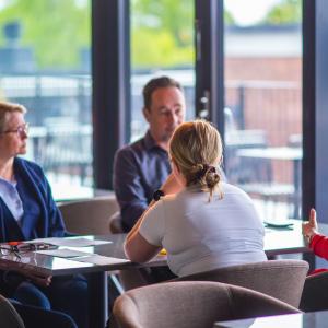 Kuvassa viisi henkilöä istuu pöydän ääressä.