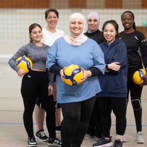 Kuusi naista lentopallokentällä ryhmäkuvassa. Kolmella heistä on lentopallo kädessään. 