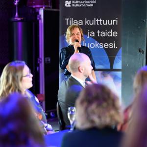 Karoliina on mikrofoni kädessään puhumassa uudistuneen Kulttuuripankin julkistamistilaisuudessa 30.9.2025