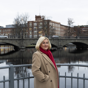 Henkilö seisoo metallikaiteen edessä. Takana näkyy koskea, Satakunnansilta autoineen ja Tampellan rakennuksia.