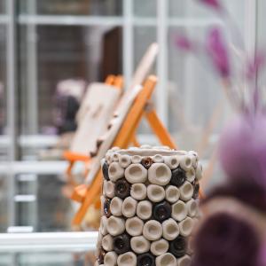 Savitöitä lasisessa vitriinissä. Keskellä ruukku ja sivussa hahmoa esittävä teos.