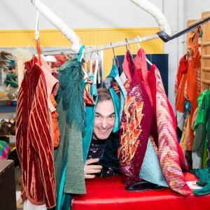 Mies kurkistaa värikkäiden vaatteiden välistä.