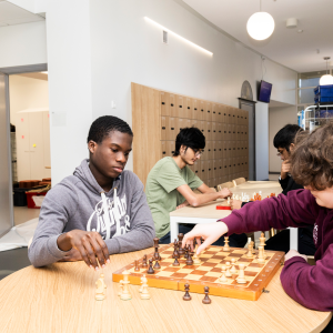 Four people are playing chess, two in the front and two in the back, using the chessboard on the table.