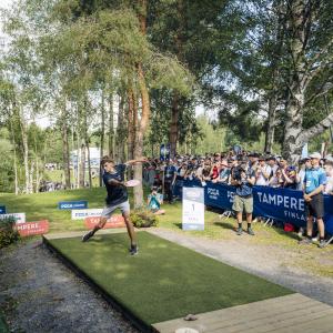 Pelaaja heittää frisbeegolf-kiekkoa yleisön katsellessa.