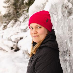 Punapipoinen henkilö nojaa jäiseen korkeaan kallioon.