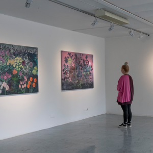 Henkilö katsoo värikkäitä ja suuria kukkatauluja taidegalleriassa.