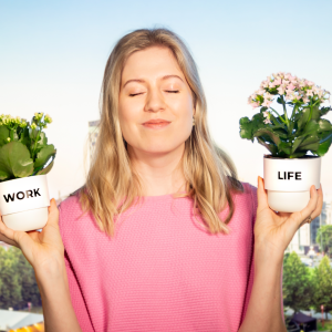 Henkilö on silmät kiinni ja pitelee molemmissa käsissään kukkaruukkuja tasapainossa. Toisessa kukkaruukussa lukee work ja toisessa life. Takana Tampereen kaupunkimaisema.