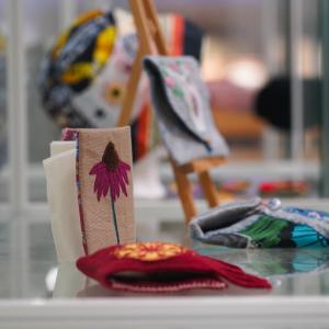 Vitriini, jossa on kirjontatöitä. Etualalla kukka-aiheinen työ.