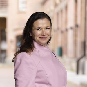 Maria Nikkilä katsoo hymyillen kameraan päällään vaaleanpunainen villakangastakki. 