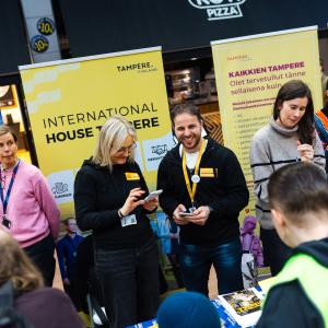 Useita hymyileviä kaupungin työntekijöitä asukasillan esittelypisteillä. Heidän takanaan on värikkäitä roll-upeja.