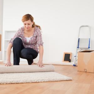 Nainen käärii mattoa rullalle ja vieressä on pahvilaatikkoja sekä tikapuut.