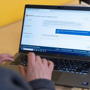 A person is studying the Entrepreneurship Advisory website on a laptop. The person is photographed from behind, with only a bit of hair, the right shoulder, and the hand visible. On the laptop screen, the webpage of the new service is displayed.