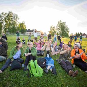 Innostuneita, iloisia aikuisia ilta-auringossa istumassa nurmella.