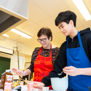 Kaksi henkilöä on leivontatarvikkeiden ääressä esiliinat edessään.