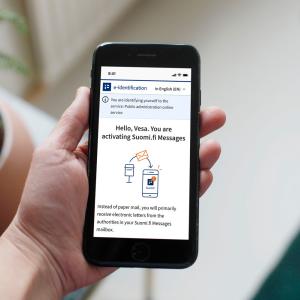 A person is holding a phone, and the screen displays instructions on how to set up Suomi.fi messages.