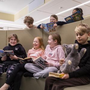 The children are sitting on a cushioned bench, reading books and laughing.