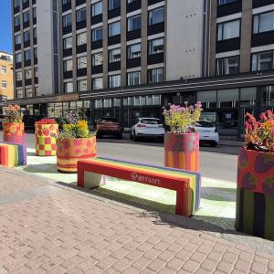 Rainbow-colored concrete benches, large plant pots with berry-themed paintings, and asphalt painted to look like a picnic blanket on Hallituskatu.
