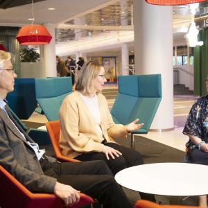 Kolme senioria istuu pyöreän pöydän ääressä keskustelemassa.