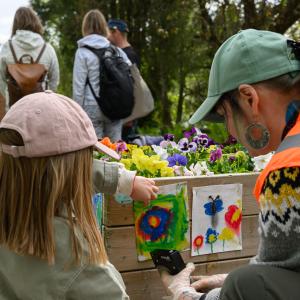 Two people wearing baseball caps are looking at the watercolor paintings on the side of the planter.