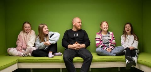 Oppilaita ja opettaja istuu penkillä hymyilevinä.