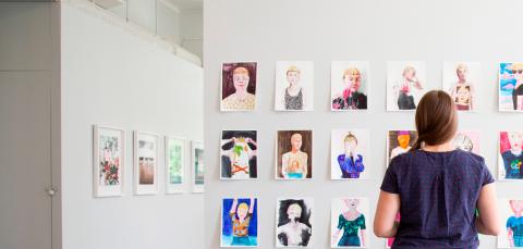 Henkilö katselee seinälle kiinnitettyjä taideteoksia.