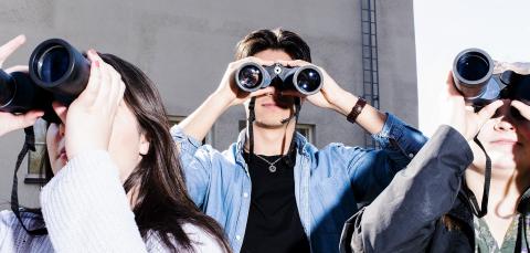 Kolme opiskelijaa katselee kiikareilla.