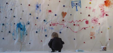 Pieni tyttö maalaa seinään vesivärillä.